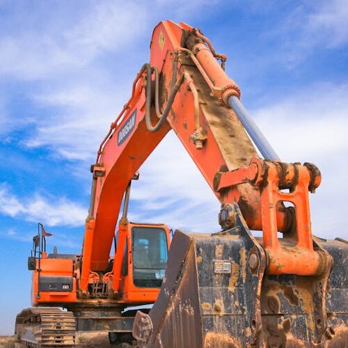 pexels-photo-1078884-1078884 A large orange excavator working on a construction site under a blue sky.