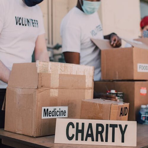 pexels-photo-6647119-6647119 Group of volunteers wearing masks organizing donation boxes labeled food and medicine outdoors.