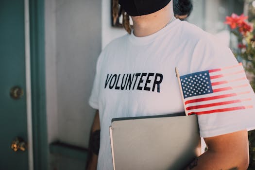 Volunteer wearing a mask holds a notebook and American flag, symbolizing community service.